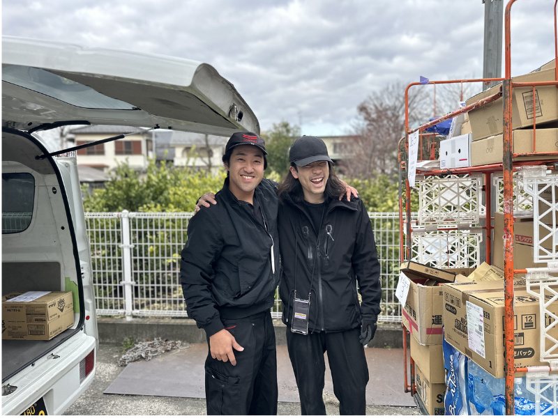 配送現場で笑顔で並ぶ株式会社IYABIのドライバー2人と軽バン