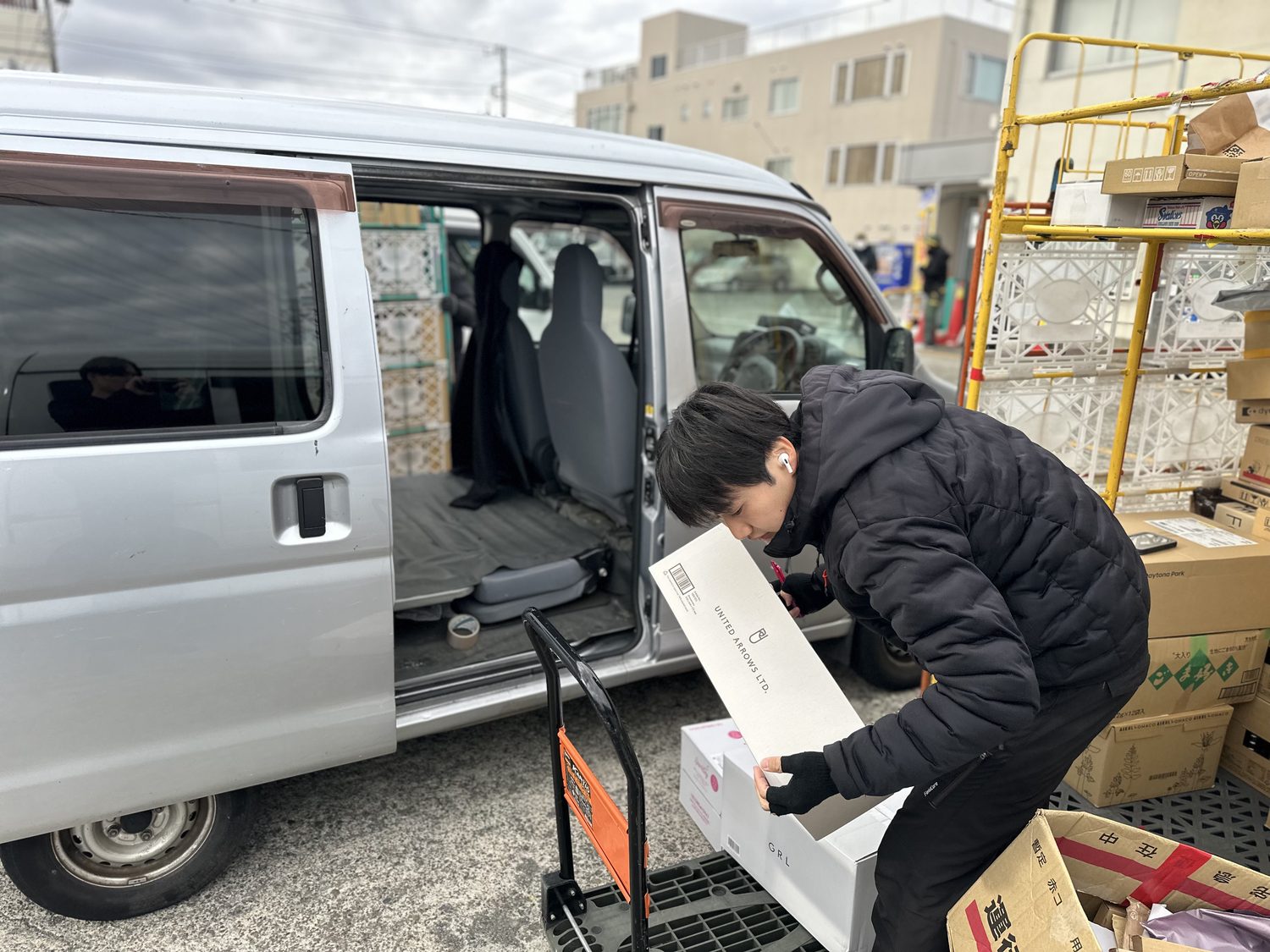 軽バンの横で台車を使い段ボールを積み込む株式会社IYABIのドライバー